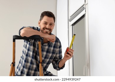 Man with measure tape on stepladder near window indoors. Roller blinds installation - Powered by Shutterstock