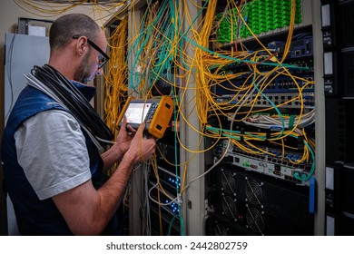 A man measures the optical signal level in a server room. A technician repairs faults in a fiber optic network using a reflectometer. - Powered by Shutterstock