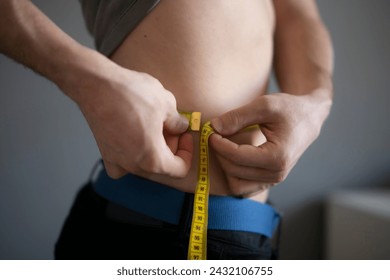 Man Measures Waist Circumference With Yellow Tape During Fitness Check - Powered by Shutterstock