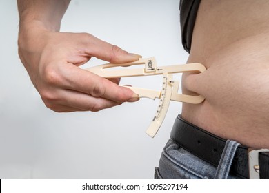 Man is measuring body fat on his belly with caliper.
