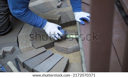 Man measuring and marking bricks for a decorative two tone paver pattern in front a stairway.