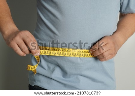 Man measuring waist with tape on grey background, closeup