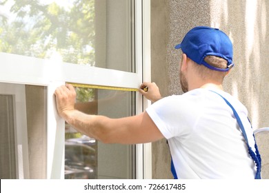 Man Measuring Window Prior To Installation Of Roller Shutter Outdoors