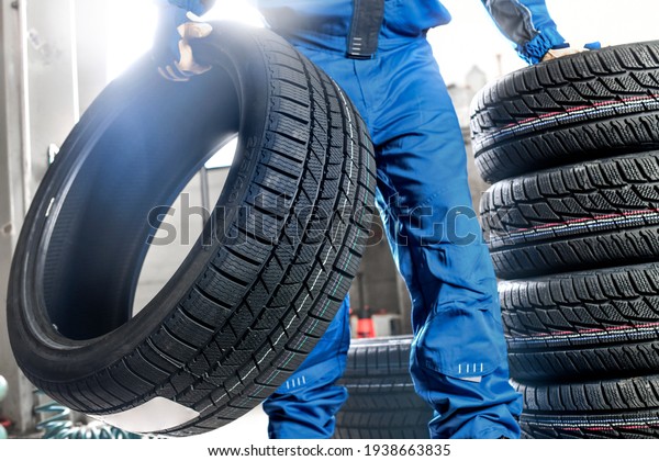 Man mechanic with car tire in service\
center. Changing tire\
maintenance.