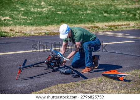 Man mechanic, rc pilot assembling remote controlled scale model helicopter on airfield runway.