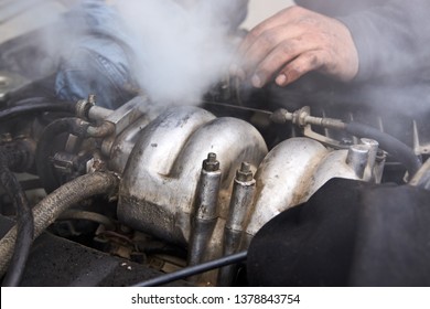 Man Mechanic Repair A Smoking Engine Of His Overheated Car. Broken Down Old Car With Smoke Or Steam From Hose. 