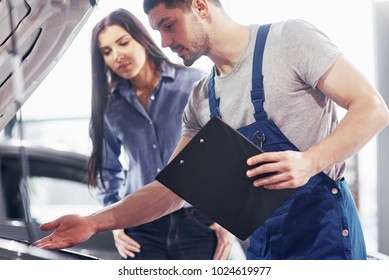 A Man Mechanic And Woman Customer Look At The Car Hood And Discuss Repairs.