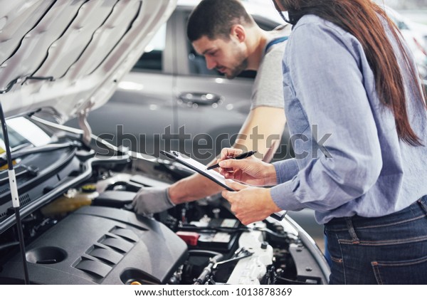 A man mechanic and woman customer look at the\
car hood and discuss repairs.
