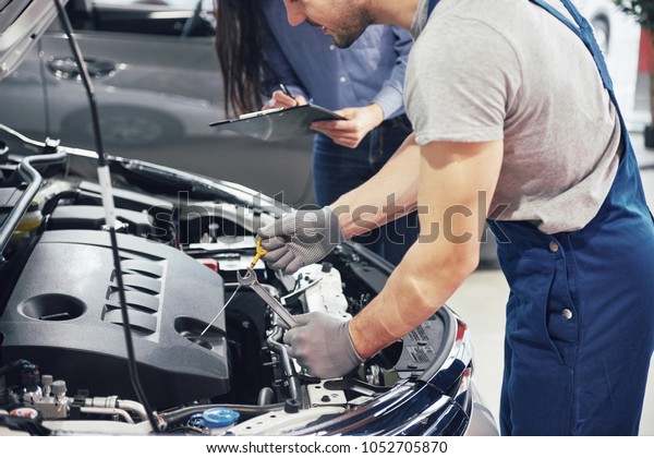 A man mechanic and woman customer look at the\
car hood and discuss repairs.