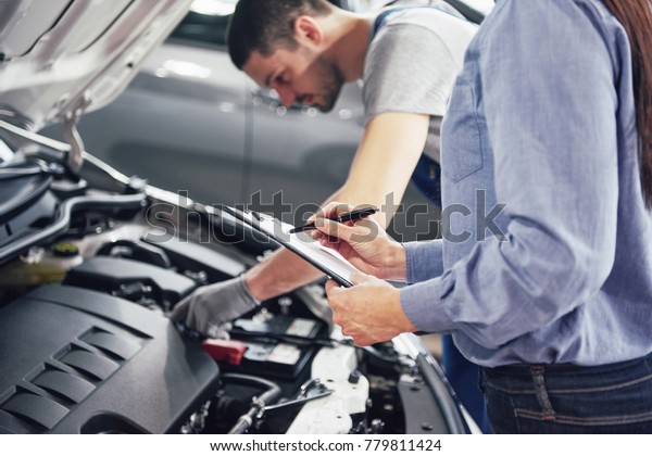 A man mechanic and woman customer look at the
car hood and discuss repairs.