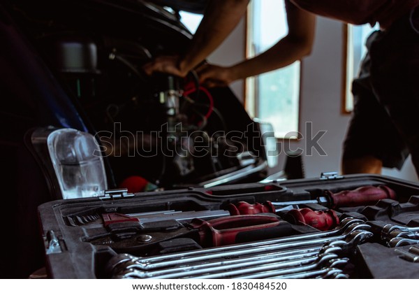 Man in mechanic workshop fixing car with tools\
in foreground
