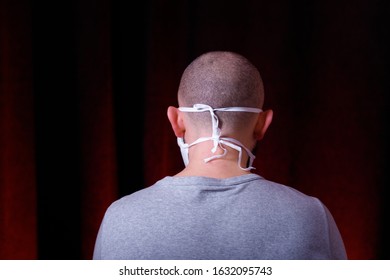 A Man In Medical Gauze Mask Standing Back To Camera On Dark Red Background. Virus Preventive Methods. Protection Of Upper And Lower Respiratory System From  Chinese Coronavirus Concept.