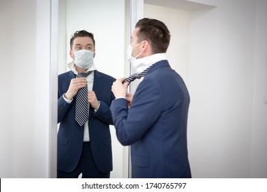 Man In A Medical Mask Corrects His Tie In Front Of The Mirror During The Covid-19 Pandemic. Concept Of Returning To Work After Reopening The Economy.