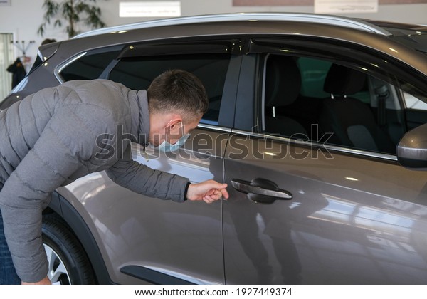 A man in a medical mask examines a car\
in the cabin for defects. Car rent. Buying a\
car