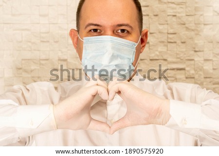A man with a medical mask and hands in a latex glove shows a heart symbol. Doctor for the heart. Love for our pancreas. Love our healthcare professionals