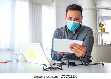 Man in a medical mask at the office. Man works remotely. The guy uses a tablet PC and a laptop for work, and medicine mask and antiseptic for self protective. Coronavirus pandemic, influenza, covid19 - Powered by Shutterstock