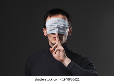 Man with medical mask on his eyes showing secret finger gesture. Concept of anti vaxxer and disinformation during global virus pandemic.
