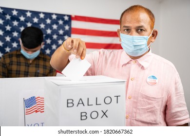 Man In Medical Mask Placing Ballot Paper Inside The Ballot Box While Looking At Camera - Concept Of In Person Voting And People Busy At Polling Booth At US Election