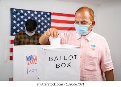 Man In Medical Mask Placing Ballot Paper Inside The Ballot Box - Concept Of In Person Voting And People Busy At Polling Booth At US Election