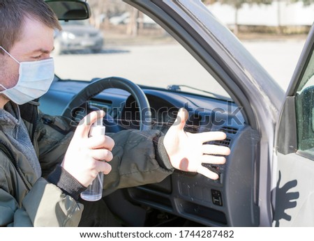 A man in a medical mask sits in a car and sprays antiseptic on his hands.