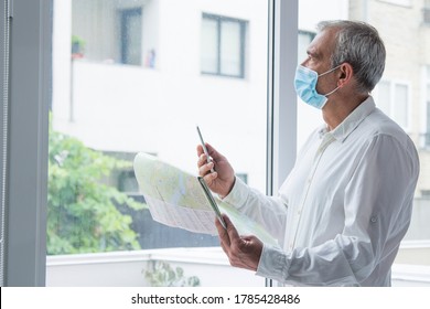 Man In Medical Mask With A World Map In His Hand And In The Other The Mobile Phone, Concept Of Travel In The New Normal