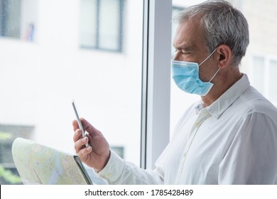 Man In Medical Mask With A World Map In His Hand And In The Other The Mobile Phone, Concept Of Travel In The New Normal