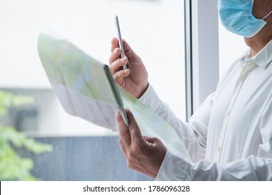 Man In Medical Mask With A World Map In His Hand And In The Other The Mobile Phone, Concept Of Travel In The New Normal