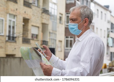 Man In Medical Mask With A World Map In His Hand And In The Other The Mobile Phone, Concept Of Travel In The New Normal