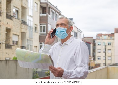 Man In Medical Mask With A World Map In His Hand And In The Other The Mobile Phone, Concept Of Travel In The New Normal