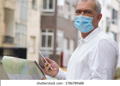 Man In Medical Mask With A World Map In His Hand And In The Other The Mobile Phone, Concept Of Travel In The New Normal