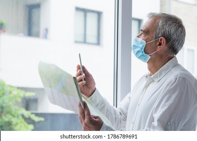 Man In Medical Mask With A World Map In His Hand And In The Other The Mobile Phone, Concept Of Travel In The New Normal