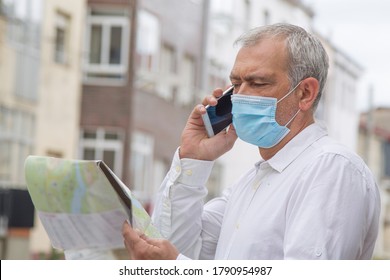 Man In Medical Mask With A World Map In His Hand And In The Other The Mobile Phone, Concept Of Travel In The New Normal