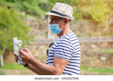 Man In Medical Mask With A World Map In His Hand And In The Other The Mobile Phone, Concept Of Travel In The New Normal