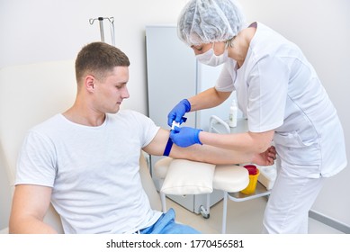 man in medical office gives blood. doctor puts tourniquet on his arm