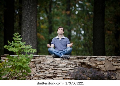 Man is meditating on stone ball in forest. Outdoor meditation surrounded by nature in yoga pose. Maintaining peace and quiet. Inner harmony. Time alone with yourself. Self-isolation. Survive stress - Powered by Shutterstock