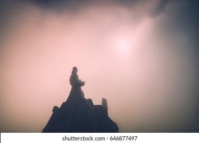 Man Meditating In Sitting Yoga Position On The Top Of A Mountain Above Clouds At Sunset Light. Zen, Meditation, Peace. Instagram Stylization.