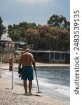 A man with a metal detector searches for gold and other valuables on the beach in Athens in summer.  Vertical photo view from the back.