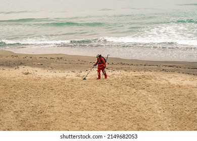 Man With A Metal Detector Walks Along The Beach In A Red Suit. Slow Motion, 4k, Slow Motion