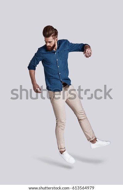 Man in mid-air.  Full\
length of handsome young man looking down while jumping against\
grey background