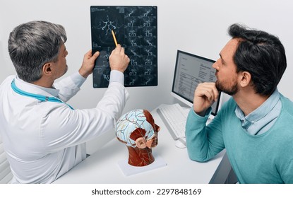 Man with migraine and headache at consultation with neurologist who looking at MRA of patient's head to analyze his brain health. Cerebrovascular MRI