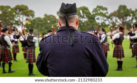 Man in military jacket watching bagpipe band. 
