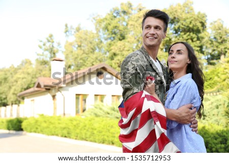 Man in military uniform with American flag hugging his wife outdoors