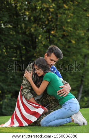 Man in military uniform with American flag hugging his wife at green park