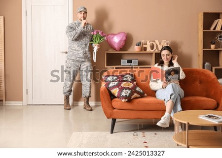 Man in military uniform with bouquet of flowers sneaking to surprise his wife at home. Valentine's Day celebration