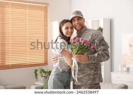 Man in military uniform greeting his wife with bouquet of flowers at home. Valentine's Day celebration