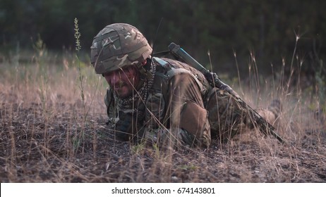 Man In Military Uniform With Gun Crawling Alone On Ground In Field.