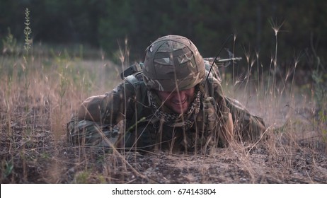 Man In Military Uniform With Gun Crawling Alone On Ground In Field.