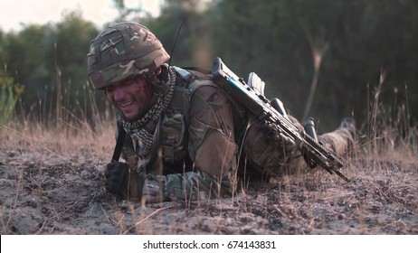 Man In Military Uniform With Gun Crawling Alone On Ground In Field.