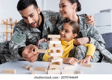 Man In Military Uniform Playing Blurred Wood Blocks Game Near Wife And Kid At Home