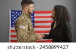 A man in military uniform shaking hands with a woman in an office, with the us flag in the background.